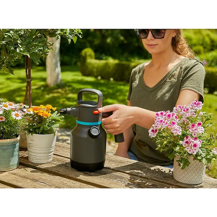 Gardena Drucksprüher - 1,25 l - Eine Frau benutzt einen Gardena Drucksprüher zum Gießen von Blumen auf einem Holztisch im Garten.
