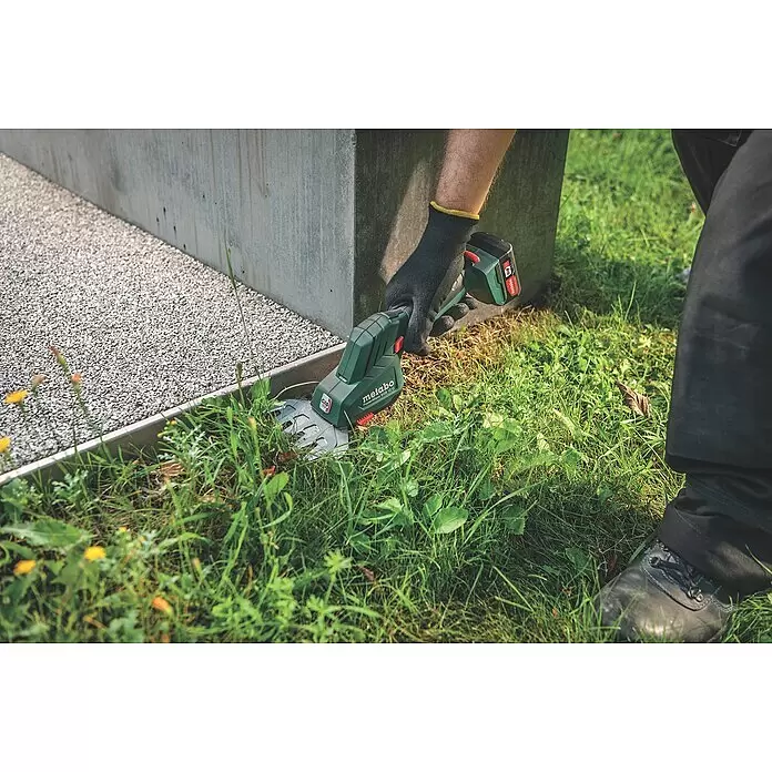 Metabo Akku-Gras- & Strauchschere PowerMaxx SGS 12 Q - 12 V, Li-Ionen, Ohne Akku, Schwertbreite: 13 cm - Grüne und schwarze Akku-Gras- und Strauchschere trimmt Gras entlang einer Beton- und Kieskante.
