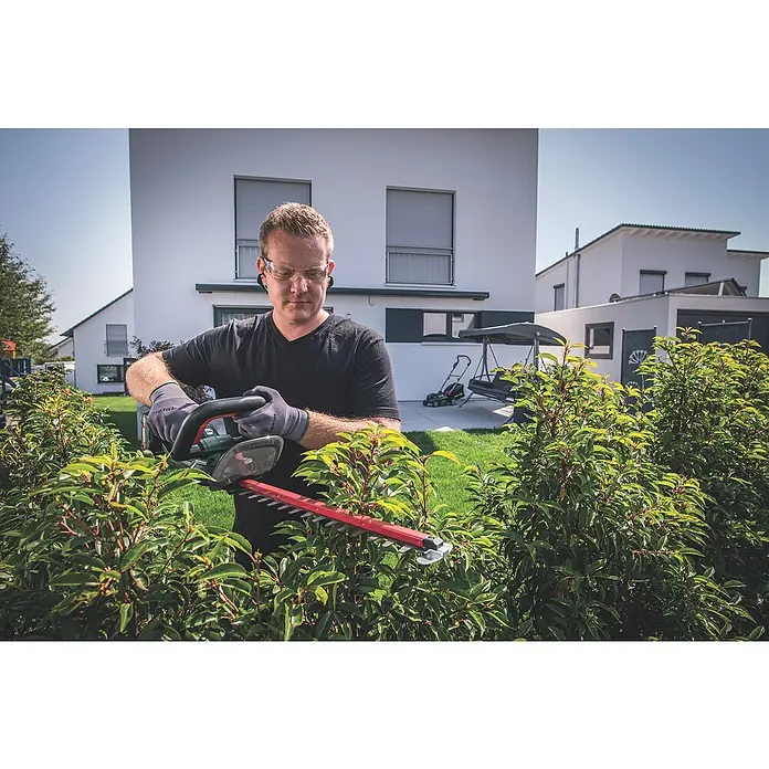 Metabo CAS 18V Akku-Heckenschere HS 18 LTX 45 - 18 V, Li-Ionen, Ohne Akku, Schwertlänge: 45 cm - Ein Mann, der eine Heckenschere benutzt, um die Hecke in seinem Garten zu schneiden. Die Heckenschere ist rot und schwarz und hat eine lange Klinge.
