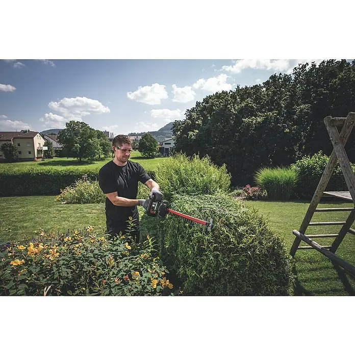 Metabo CAS 18V Akku-Heckenschere HS 18 LTX 55 - 18 V, 2 Akkus, Schwertlänge: 55 cm - Ein Mann trimmt mit einer Heckenschere eine grüne Hecke im Garten, wobei er eine Schutzbrille und Handschuhe trägt.