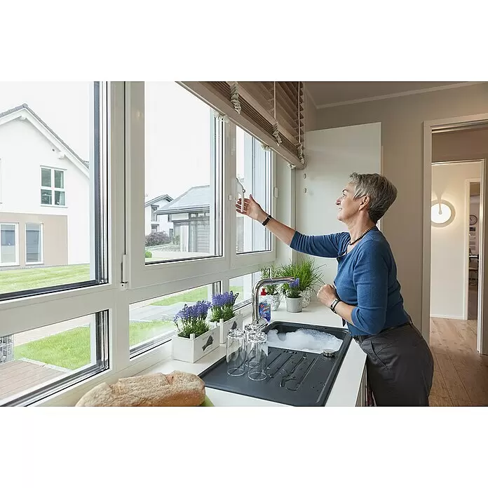 Abus Alarm-Fenstergriff FG300 - Silber - Frau verstellt eine hellbraune Fensterjalousie über einer Küchenspüle, um Licht und Privatsphäre zu regulieren.