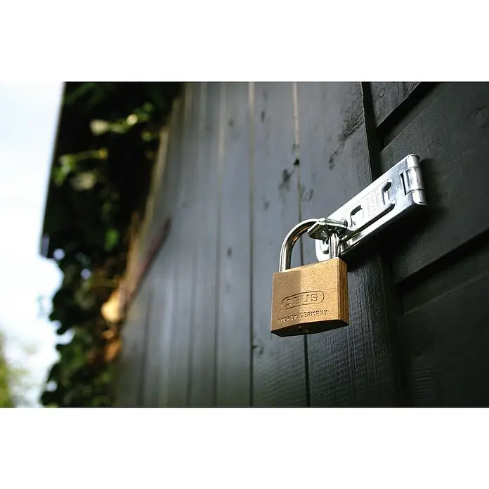 Abus Vorhängeschloss 85/40 HB40 Gleichschließend - B x H: 40 x 62 mm, Bügelstärke: 6,5 mm, Material Bügel: Gehärteter Spezialstahl - Nahaufnahme eines ABUS-Vorhängeschlosses, das an einer Schließe befestigt ist, die an einer dunklen Holztür oder einem Schuppen angebracht ist.