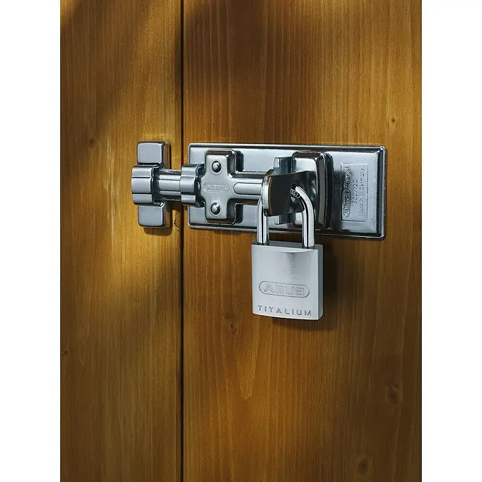 Abus Vorhängeschloss Titalium 86TI/45 - B x H: 46,5 x 96,5 mm, Bügelstärke: 8 mm, Titalium-Spezialaluminium - Nahaufnahme eines ABUS Titalium Vorhängeschlosses, das eine silberne ABUS Riegelschließe an einer Holztür sichert. Robuster Schutz für Ihr Eigentum.