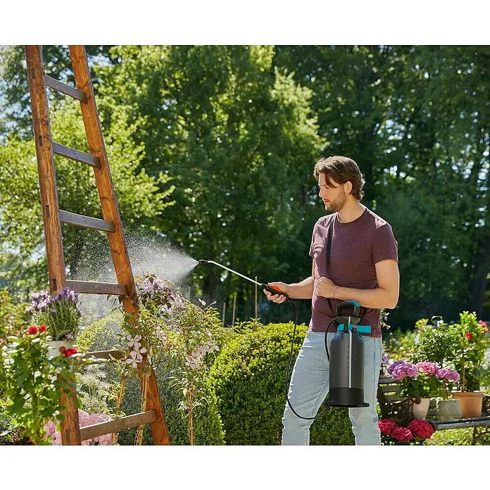 Gardena Comfort Drucksprüher - Füllmenge: 5 l, Grau - Ein Mann benutzt einen Gardena Drucksprüher, um Pflanzen zu gießen. Der Sprüher ist schwarz mit einem blauen Griff und hängt an einem Gurt.