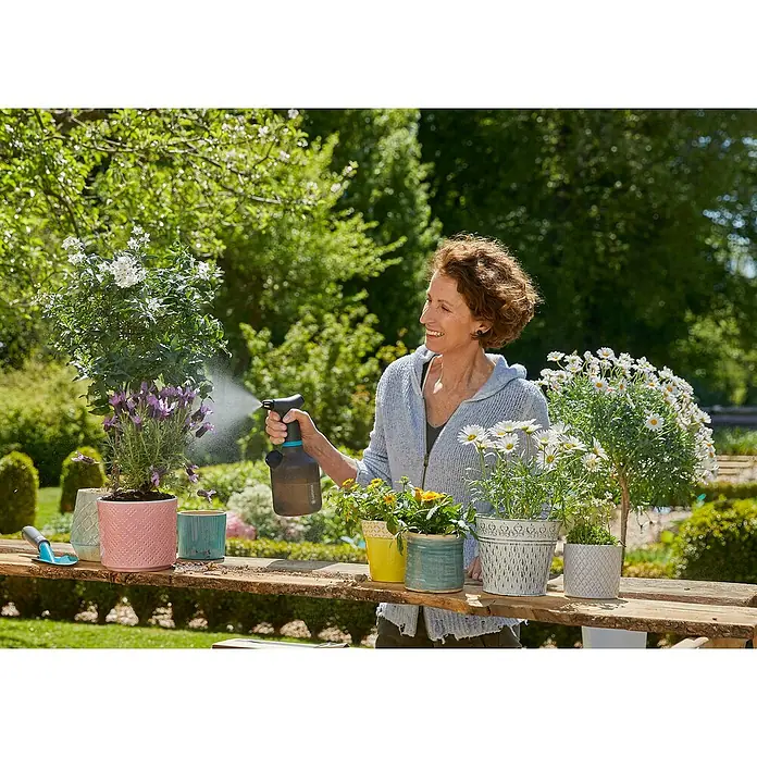 Gardena Handsprüher Easy Pump1 l - Frau gießt Pflanzen in Töpfen mit einer GARDENA-Sprühflasche auf einem Gartentisch im Freien.