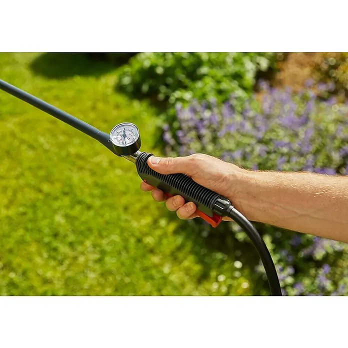 Gardena Drucksprüher Plus - Füllmenge: 12 l - Nahaufnahme der Hand einer Person, die den Griff einer Gartenspritze mit Manometer hält, vor einem Hintergrund von grünem Gras und Blumen.