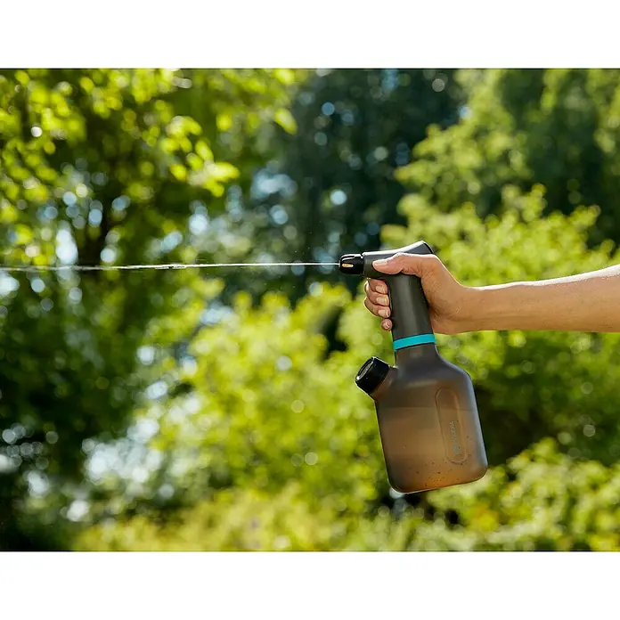 Gardena Handsprüher Easy Pump1 l - Eine Person benutzt einen Gardena Akku-Drucksprüher für Pflanzenpflege. Das Gerät ist grau und blau, im Hintergrund grüne Bäume.