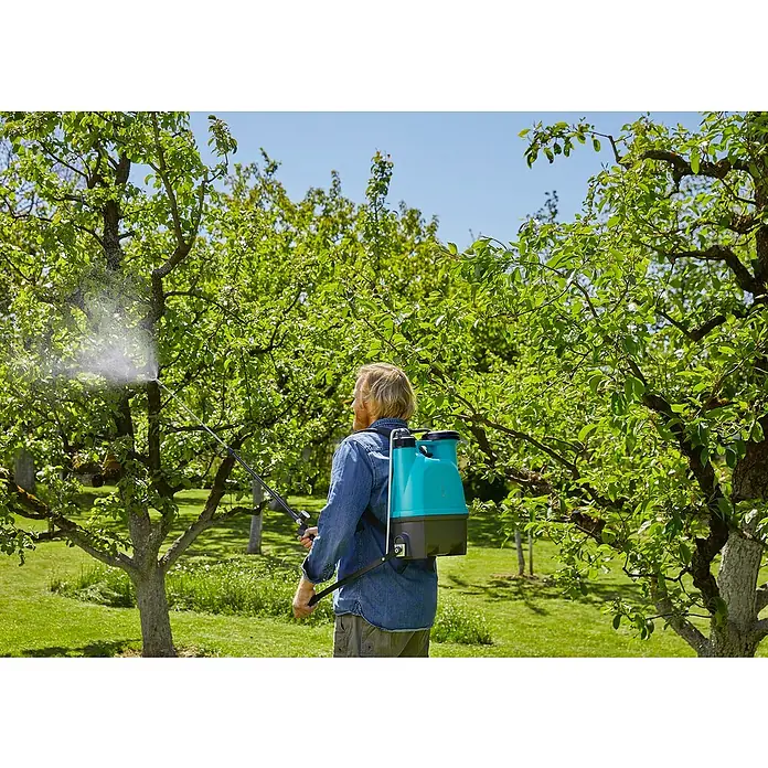 Gardena Drucksprüher Plus - Füllmenge: 12 l - Eine Person sprüht mit einem akkubetriebenen Rückensprühgerät Bäume auf einer grünen Wiese.