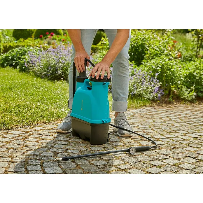 Gardena Drucksprüher Plus - Füllmenge: 12 l - Der Gardena Akku-Drucksprüher wird im Garten von einer Person bedient. Das Gerät ist blau-schwarz und hat einen Schlauch mit Messgerät.