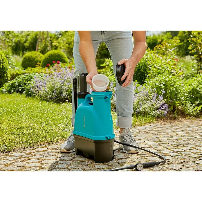 Gardena Drucksprüher Plus - Füllmenge: 12 l - Eine Person befüllt einen GARDENA Drucksprüher im Garten, umgeben von Grün. Der Sprüher steht auf einem Steinweg.