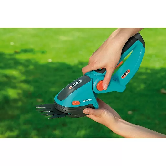 Gardena Ersatzmesser - Passend für: Gardena ClassicCut Akku-Grasschere, Gardena ComfortCut Akku-Grasschere - Hände halten eine türkis-schwarze Gardena ComfortCut Akku-Grasschere mit orangefarbenen Akzenten, einsatzbereit.