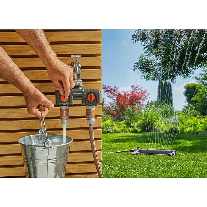 Gardena SB-System Hahnverbinder Perlstrahl - Verbindung von Schläuchen, Kunststoff - Gardena Wasserverteiler im Einsatz: Ein Hahn füllt einen Eimer, während ein Rasensprenger den Garten bewässert.
