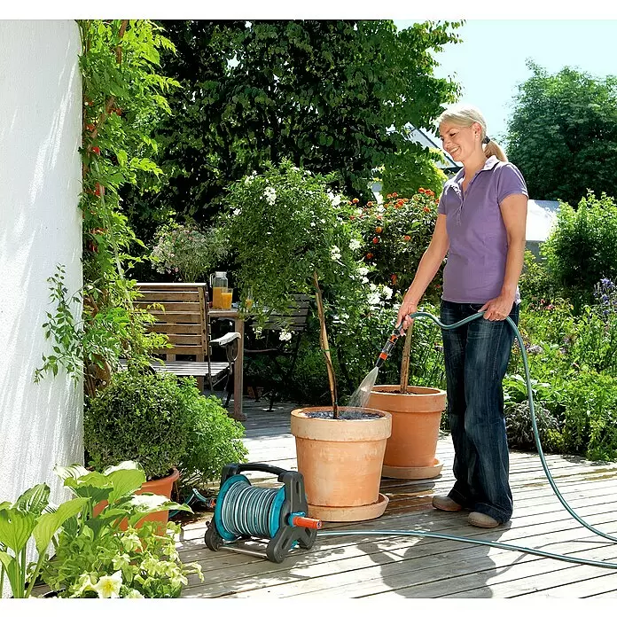 Gardena Classic Schlauchtrommel - Kunststoff, Schlauchlänge: 10 m - Graue und türkise Gardena Schlauchbox mit Schlauch, den eine Frau zum Gießen von Pflanzen auf einer Holzterrasse verwendet.