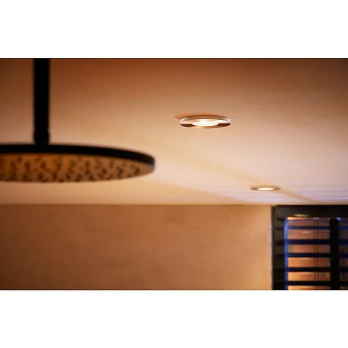 Philips Hue LED-Einbauleuchte rund Xamento White & Color Ambiance - 5,5 W, Ø x H: 93 mm x 10 cm, Chrom, Transparent, RGBW, IP44 - Das Bild zeigt eine elegante Deckenleuchte mit einem modernen Design, die eine angenehme und warme Beleuchtung erzeugt.
