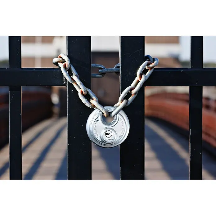 Abus Diskusschloss 25/70 Gleichschließend - B x H: 70 x 70 mm, Bügelstärke: 10 mm, Edelstahl - Das Bild zeigt ein Abus Diskus Vorhängeschloss mit einer Kette an einem schwarzen Metallgitter, das einen sicheren und robusten Eindruck macht.