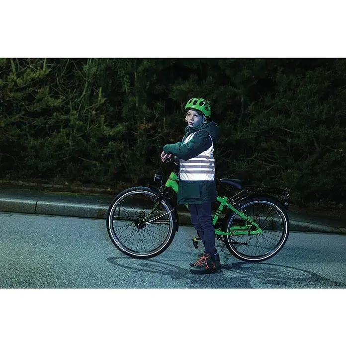 Abus Kinder- & Jugendwarnweste Max - Grau, Größe: S 48 – 54 cm - Ein Kind mit grünem Fahrradhelm und reflektierender Weste steht neben einem grünen Fahrrad auf der Straße. Die Fahrradbeleuchtung sorgt für Sicherheit.