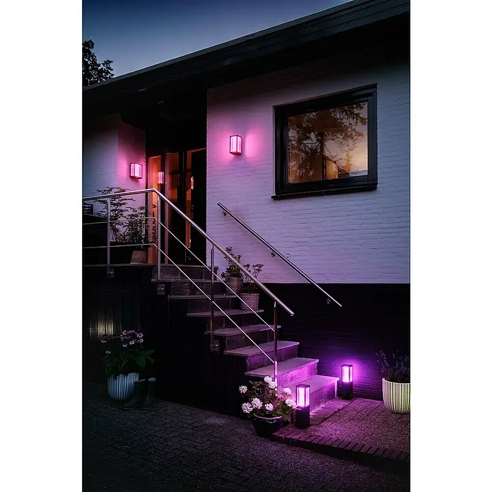 Philips Hue LED-Außenwandleuchte Impress - 8 W, 11,7 x 19 x 24 cm, Schwarz, IP44 - Dieses Bild zeigt Außenleuchten, die ein Haus mit lila Licht beleuchten, wodurch eine einladende und moderne Atmosphäre entsteht.
