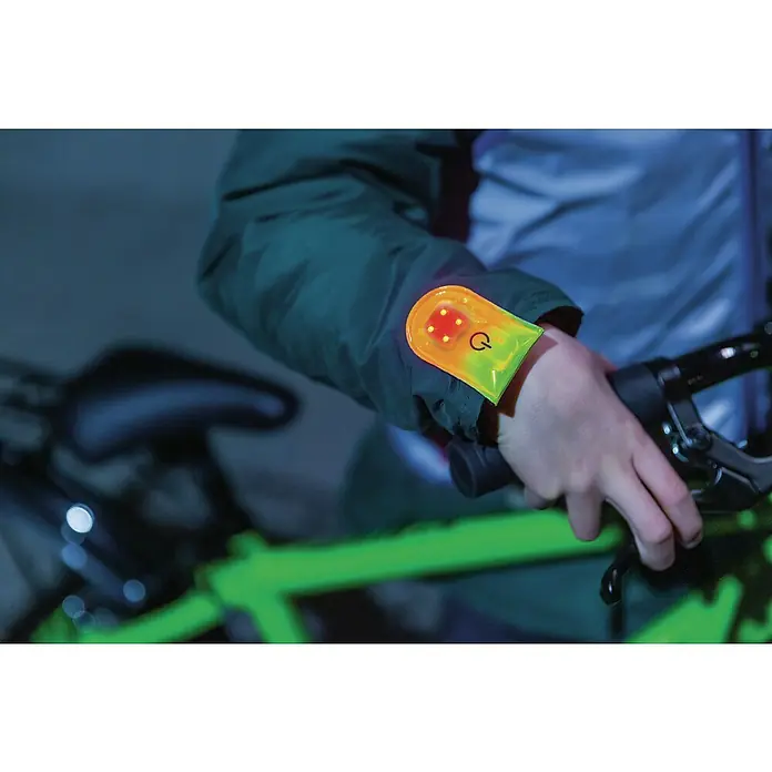 Abus LED-Leuchte Linus - Gelb - Person mit reflektierendem Armband und LED-Leuchten am Arm, während sie ein Fahrrad hält. Das Armband erhöht die Sichtbarkeit.