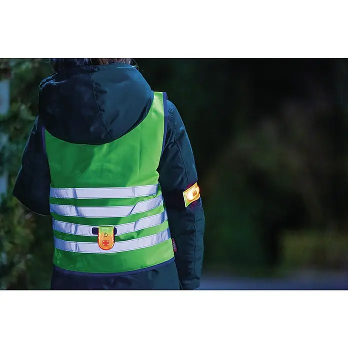 Abus LED-Leuchte Linus - Gelb - Eine Person trägt eine leuchtend grüne Warnweste mit reflektierenden Streifen und einem blinkenden Licht für bessere Sichtbarkeit.