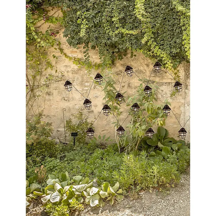 Globo Solar-Lichterkette - Länge: 430 cm, LED - Dekorative Gartenbeleuchtung mit einer Lichterkette aus Laternen vor einer bewachsenen Mauer, die eine stimmungsvolle Atmosphäre schafft.