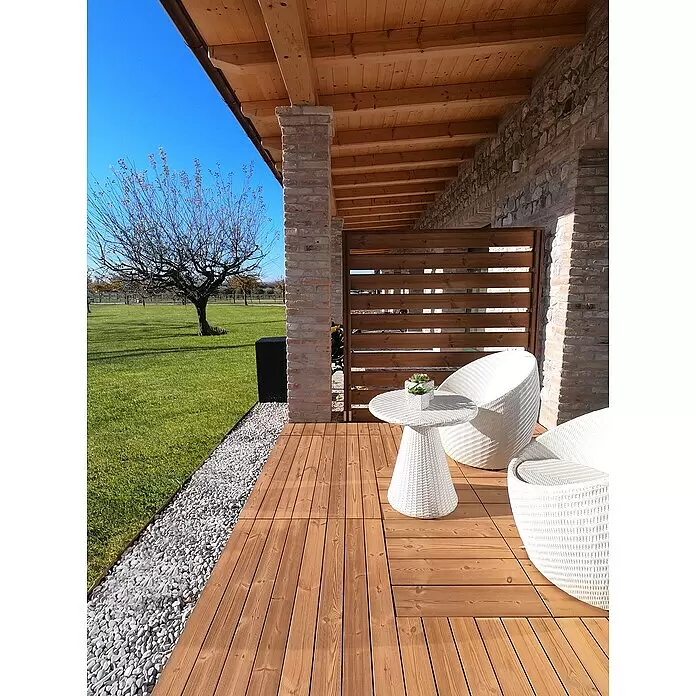 Klickfliese Smartdeck - Kiefer, 60 x 30 x 2,5 cm, Naturbraun, 1 Stk. - Außenterrasse mit modularen Holzterrassenfliesen, weißem Korbtisch und zwei Stühlen, an einem Kiesweg und Rasen.