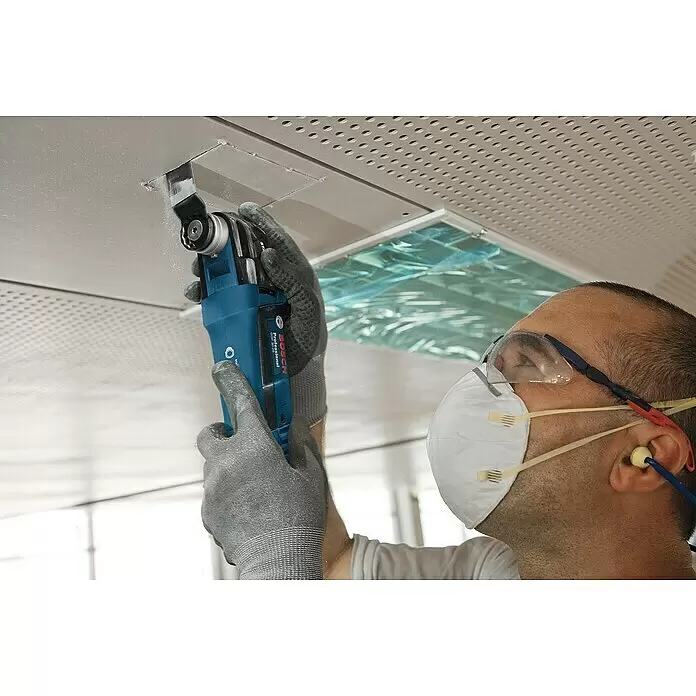 Bosch Professional Elektro-Multifunktionswerkzeug GOP 30-28 - 300 W, STARLOCK-Plus-System - Eine Person in Schutzkleidung benutzt ein blau-schwarzes Bosch Multifunktionswerkzeug, um eine rechteckige Öffnung in eine helle Deckenplatte zu schneiden.
