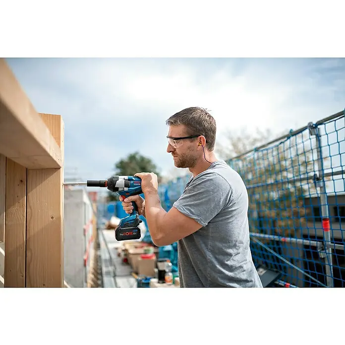 Bosch Professional AMPShare 18V Akku-Drehschlagschrauber GDS 18V-1050 H - 18 V, Ohne Akku - Ein Mann mit Schutzbrille und Ohrstöpseln benutzt einen Bosch Akku-Schlagschrauber ProCORE 18V, um eine Schraube in Holz zu drehen.