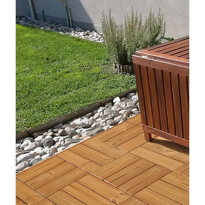 Loseta con sistema click Smartdeck - Pino, 30 x 30 x 2,5 cm, Natural, 6 ud. - Primer plano de una terraza de madera con muebles de jardín, rodeada de césped y piedras, centrado en la textura de la madera y el entorno natural.