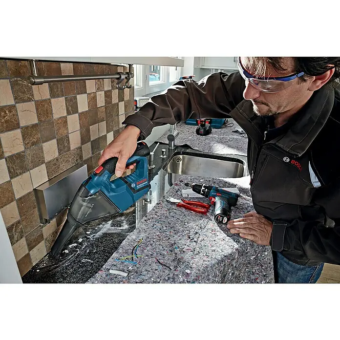 Bosch Professional Akku-Handstaubsauger GAS 12V - 12 V, Ohne Akku, Luftmenge: 15 l/s, Koffer - Ein Handwerker reinigt mit einem Bosch Akku-Staubsauger eine Arbeitsfläche, auf der auch ein Akkuschrauber liegt.