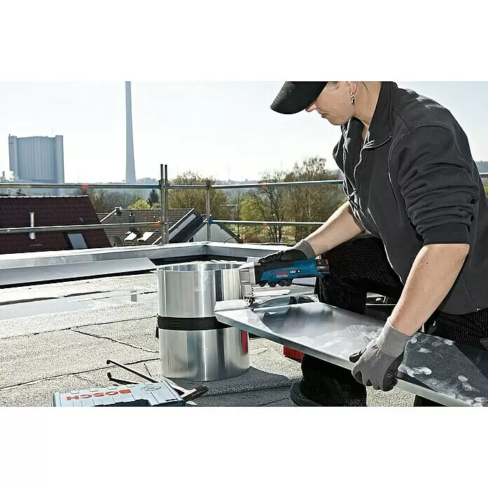 Bosch Professional Akku-Blechschere GSC 12V-13 - 12 V, Ohne Akku, Leerlaufhubzahl: 3.600 /min - Person schneidet mit blau-schwarzem Bosch Elektrowerkzeug ein silbernes Blech auf einem Dach.