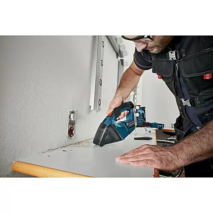 Bosch Professional Akku-Staubsauger - 12 V, 2 Akkus, Behältervolumen: 0,35 l - Mann reinigt mit einem blau-schwarzen Bosch Handstaubsauger Schmutz von einer Arbeitsplatte.