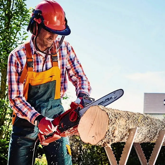 Einhell Motosierra eléctrica GH-EC 1835 - 1.800 W, Longitud de la cuchilla: 35 cm - Un hombre con equipo de seguridad serrando un tronco con una motosierra. La motosierra es una herramienta potente para trabajos de carpintería.
