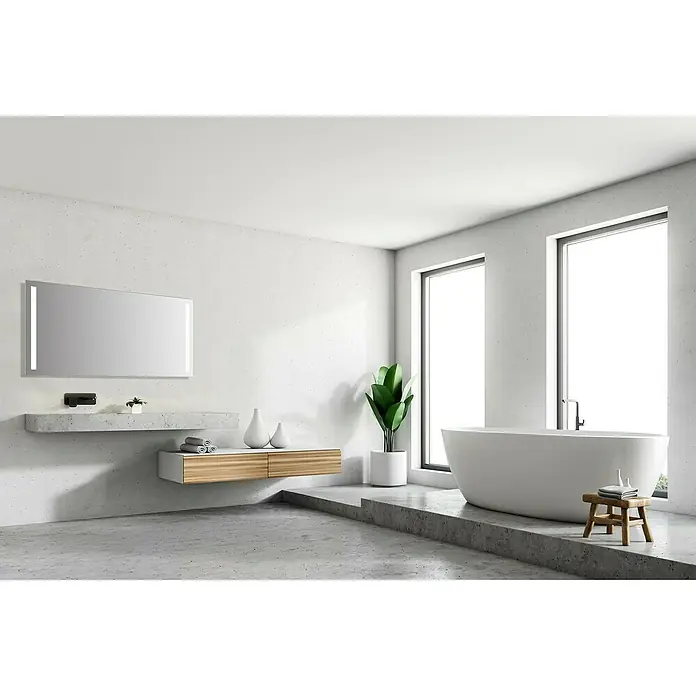 DSK Lichtspiegel Silver Dream - 140 x 70 cm - Helles Badezimmer mit freistehender Badewanne unter Fenstern, Waschtisch, Spiegel und Pflanze, die eine entspannende Atmosphäre erzeugen.