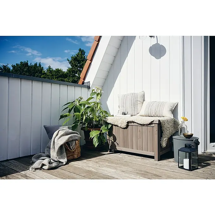 Butenkist Gartenbox Henriette - L x B x H: 75 x 45 x 45 cm, Holz, Warm Grey - Außenaufnahme einer dekorativen Holzbank mit Kissen auf einer Terrasse, die eine gemütliche Atmosphäre schafft.