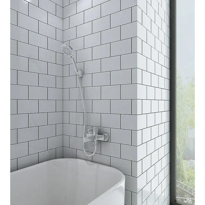 IO Dior Grifo monomando de bañera - Cromo, Brillante - Una bañera moderna con grifería plateada y ducha de mano, sobre un fondo de azulejos blancos tipo metro.