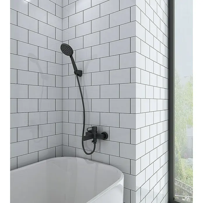 IO Dior Grifo monomando de bañera - Negro, Mate - Imagen que muestra un moderno accesorio de ducha negro montado en una pared de azulejos blancos sobre una bañera, junto a una ventana.