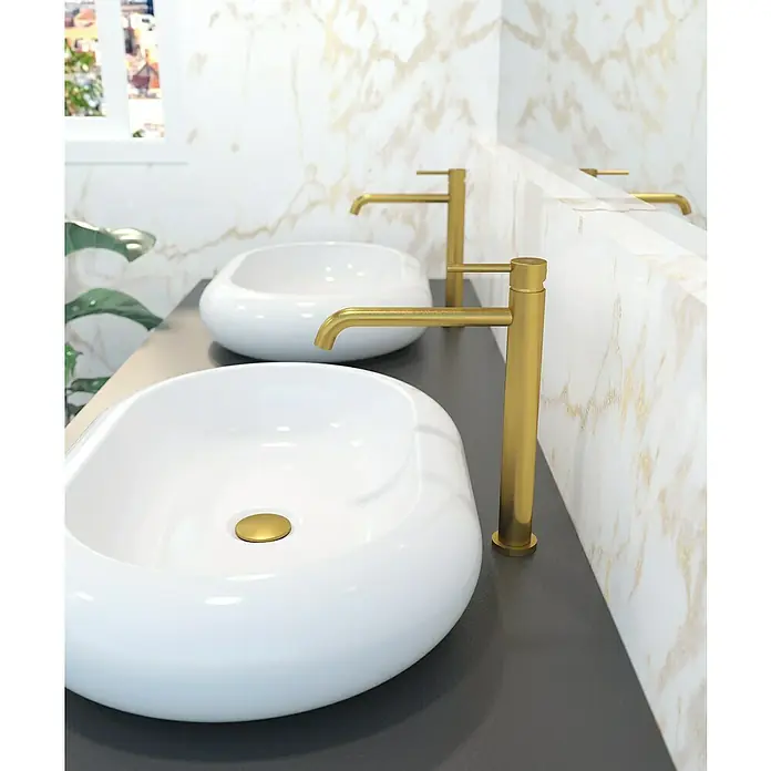 IO Sirio Grifo de lavabo - Oro - Dos lavabos sobre encimera blancos modernos con grifos dorados sobre una encimera gris. Diseño de baño elegante con pared de mármol.
