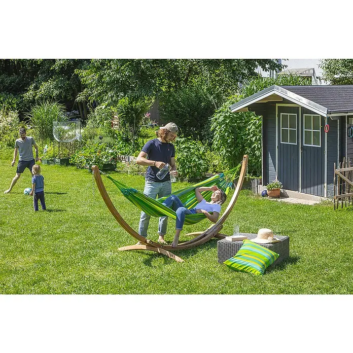 La Siesta Hängematte Brisa - L x B: 300 x 140 cm, Lime - Eine Frau entspannt in einer grünen Hängematte, während ein Mann ihr Wasser einschenkt. Im Hintergrund spielen ein Mann und ein Kind.