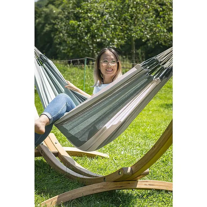 La Siesta Hängematte Modesta - L x B: 300 x 140 cm, Olive, Single - Frau entspannt in einer gestreiften Hängematte auf einem hölzernen Ständer im Garten, umgeben von Grün.