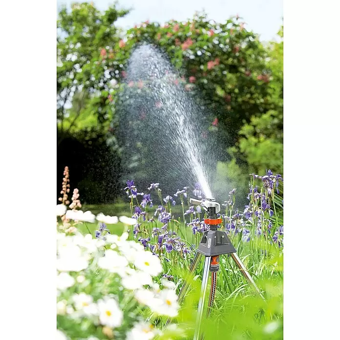 Gardena Premium Regner - Kunststoff, Beregnungssektor: 25 ° - 360 ° - Gardena Dreibeinstativ-Regner in Silber, Grau und Orange bewässert einen Garten mit lila Iris und weißen Gänseblümchen.