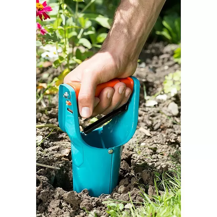 Gardena Hand-Blumenzwiebelpflanzer - Länge: 250 mm, Stahl - Eine Hand drückt einen türkis-orangen Blumenzwiebelpflanzer in Gartenerde zum Pflanzen.