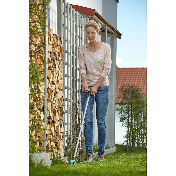 Gardena Comfort Grasschere Langstielig - Bypass, Klingenbeschichtung: Antihaftbeschichtet - Eine Frau benutzt einen Gardena Grasschneider mit langem Stiel, um Gras zu schneiden, während sie in ihrem Garten steht.