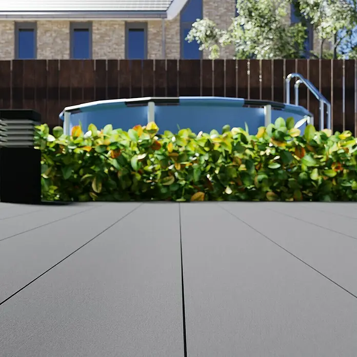 WPC-Terrassendiele300 x 19 x 1,6 cm, Grau - Ein ebenerdiger Pool mit einer grauen Terrasse im Hinterhof, umgeben von grünen Büschen, die für Privatsphäre und eine elegante Atmosphäre sorgen.