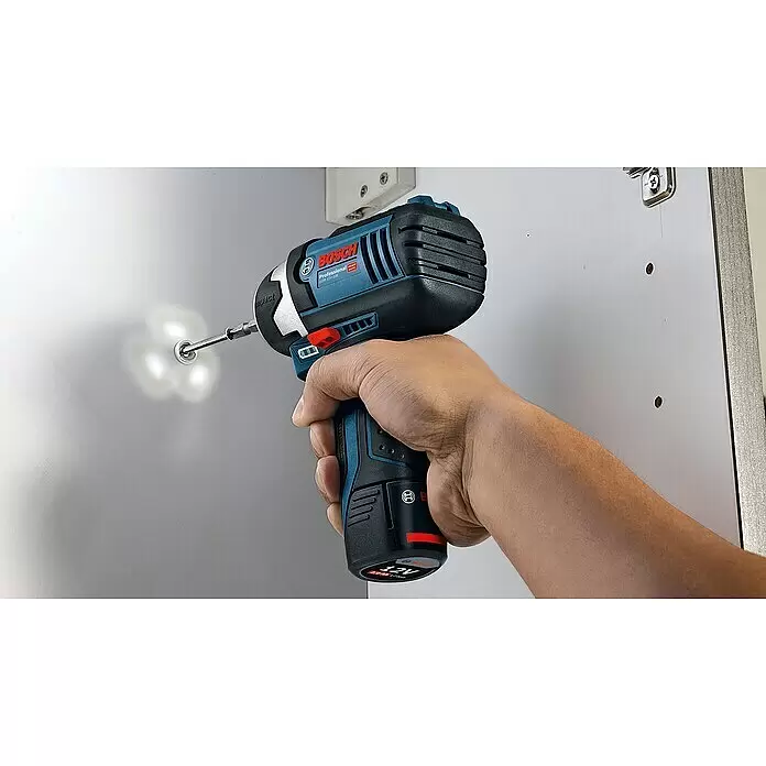 Bosch Professional Akku-Drehschlagschrauber - 12 V, Ohne Akku - Eine Hand hält einen blau-schwarzen Bosch Schlagschrauber, dessen integriertes Licht eine Schraube in einem weißen Schrank beleuchtet.