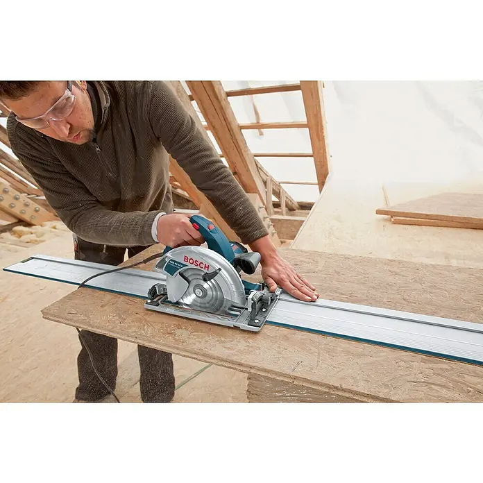 Bosch Professional Handkreissäge GKS 65 GCE - 1.800 W, Durchmesser Sägeblatt: 190 mm, Schnitttiefe bei 90 °: 65 mm - Ein Zimmermann sägt mit einer Bosch Tauchsäge GKS 65 mit Führungsschiene ein Holzbrett zu. Das Bild zeigt Präzision und professionelles Werkzeug.