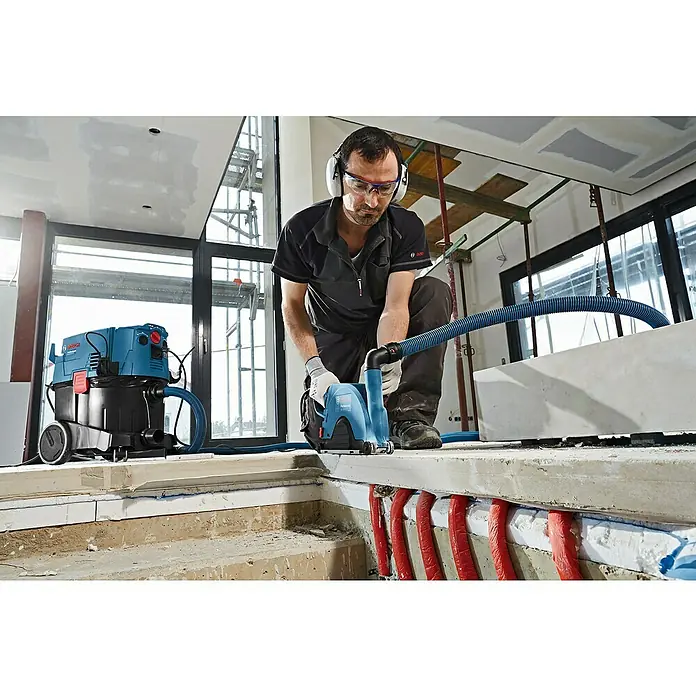 Bosch Professional Absaugvorrichtung GDE 230 FC-T - Passend für: Bosch Winkelschleifer GWS-Serie mit Ø 230 mm - Ein Bauarbeiter verwendet eine Bosch Mauernutfräse GNF 35 CA Professional mit Staubsauger zur Staubabsaugung auf einer Baustelle.
