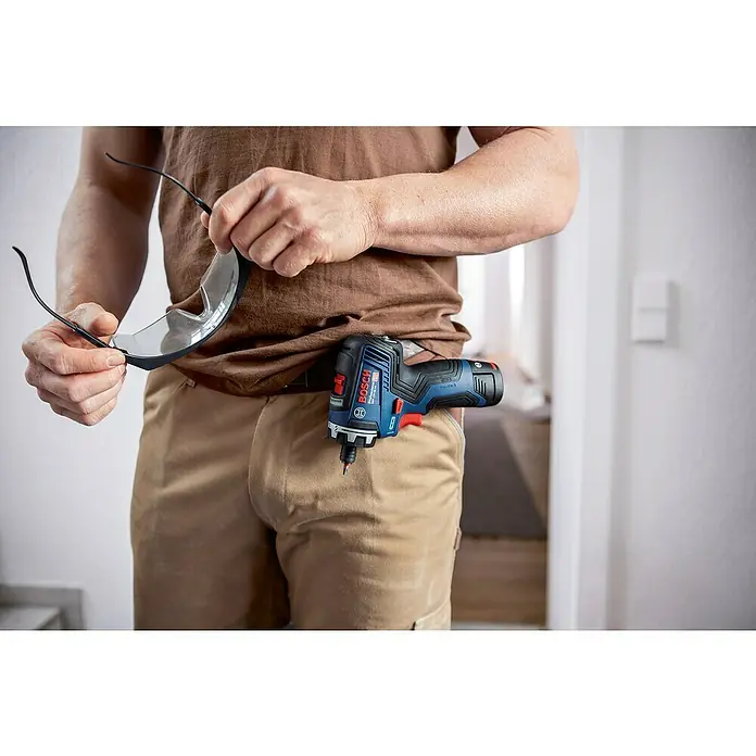 Bosch Professional AMPShare 18V Akku-Bohrschrauber-Set GSR 12V-35 HX PRO SOLO - 12 V, Ohne Akku, 35 Nm, 4 -tlg. - Der Bosch Professional Akku-Bohrschrauber ist am Gürtel befestigt, während die Person eine Schutzbrille hält.