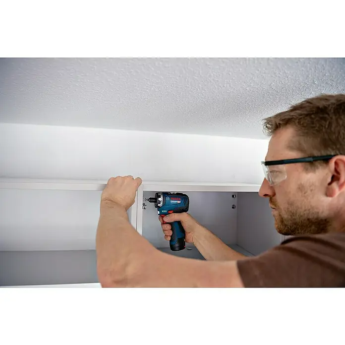 Bosch Professional AMPShare 18V Akku-Bohrschrauber-Set GSR 12V-35 HX PRO SOLO - 12 V, Ohne Akku, 35 Nm, 4 -tlg. - Ein Handwerker befestigt mit einem Bosch Akku-Bohrschrauber eine weiße Schranktür. Er trägt eine Schutzbrille für sicheres Arbeiten.