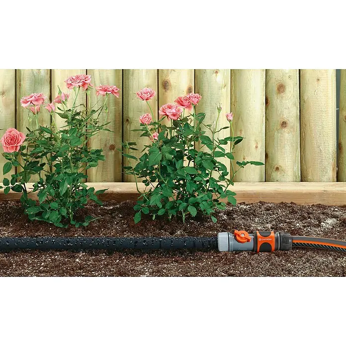 Gardena Anschlussgarnitur für Bewässerungsschlauch - Durchmesser: 13 mm, Schwarz - Nahaufnahme eines Bewässerungsschlauchs von Gardena zwischen Rosenbüschen vor einem Holzzaun.