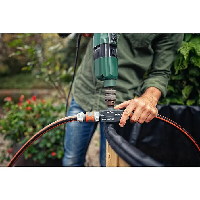 Gardena Pumpe für die Gartenbohrmaschine - Max. Fördermenge: 2.400 l/h, Kunststoff - Eine Person bohrt mit einem grünen Bohrer in einen Gardena-Schlauchverbinder, der an einen Wasserschlauch angeschlossen ist.